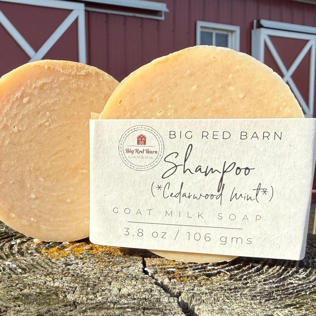 Two goat milk shampoo bars with a label in front of a red barn.