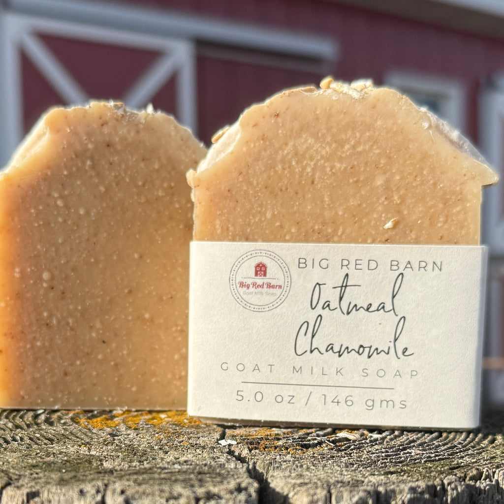 Two bars of oatmeal chamomile goat milk soap with a label in front of a red barn.