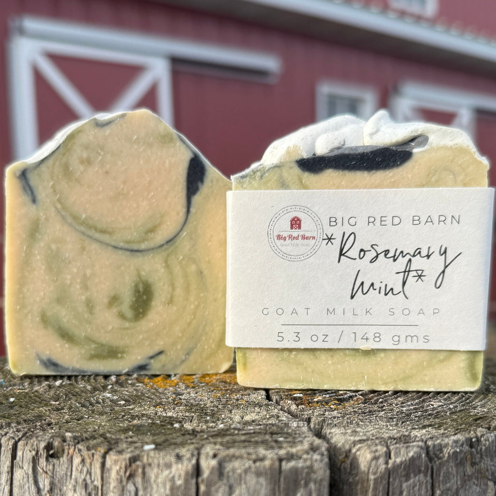 Two goat milk soaps with a label in front of a red barn.